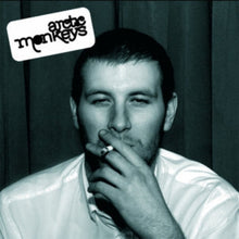 Load image into Gallery viewer, This image features the cover art for the Arctic Monkeys’ debut studio album, "Whatever People Say I Am, That’s What I’m Not," released in 2006. The album cover is a black and white photograph of the band member, Arctic Monkeys frontman Alex Turner, sitting in a dimly lit room, exuding a moody and artistic vibe.