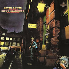 Cargar imagen en el visor de la galería, Album cover featuring a person in a costume standing on a street with neon signs and brick buildings.