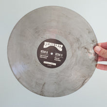 Cargar imagen en el visor de la galería, Vinyl record with a label held by a hand against a light gray background