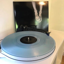 Cargar imagen en el visor de la galería, Turntable with a blue platter and a vinyl record with a black and white image of feet on a dark background.