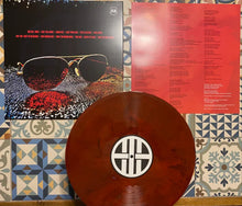 Charger l&#39;image dans la galerie, Vinyl record with a red disc and black cover featuring sunglasses, on a patterned surface.