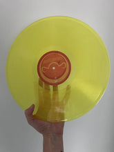 Load image into Gallery viewer, Yellow vinyl record held by a hand against a gray background