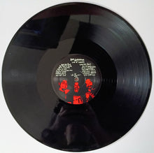 Charger l'image dans la galerie, A black vinyl record photographed from above on a white background. The center label has white printed text and a red band portrait.