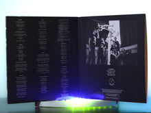 Cargar imagen en el visor de la galería, Open book with text on one side and a black and white photo on the other, illuminated by blue light.