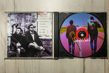 Cargar imagen en el visor de la galería, CD cover with black and white photo of two people and a colorful vinyl disc on a wooden surface