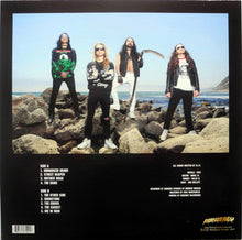Load image into Gallery viewer, Band members standing on rocks by the ocean with a black border and text.