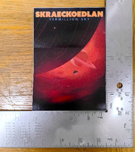 Load image into Gallery viewer, Book titled 'Skraeckoedlan Vermillion Sky' on a wooden surface with a ruler for scale.