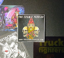 Load image into Gallery viewer, Sticker with 'The Cosmic Peddler' design on a dark surface with other stickers.
