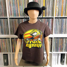Cargar imagen en el visor de la galería, A mannequin wearing a dark brown graphic t-shirt with a yellow and orange 'Truck Fighter' design, styled with a black bowler hat, set against a background of shelves filled with vinyl records.